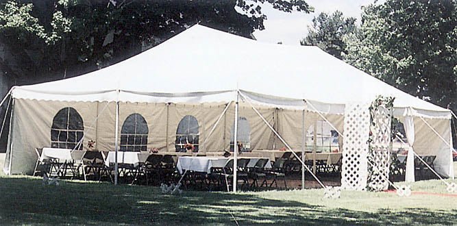 gorgeous white wedding tent set back near trees showing the front and side of the tent 1